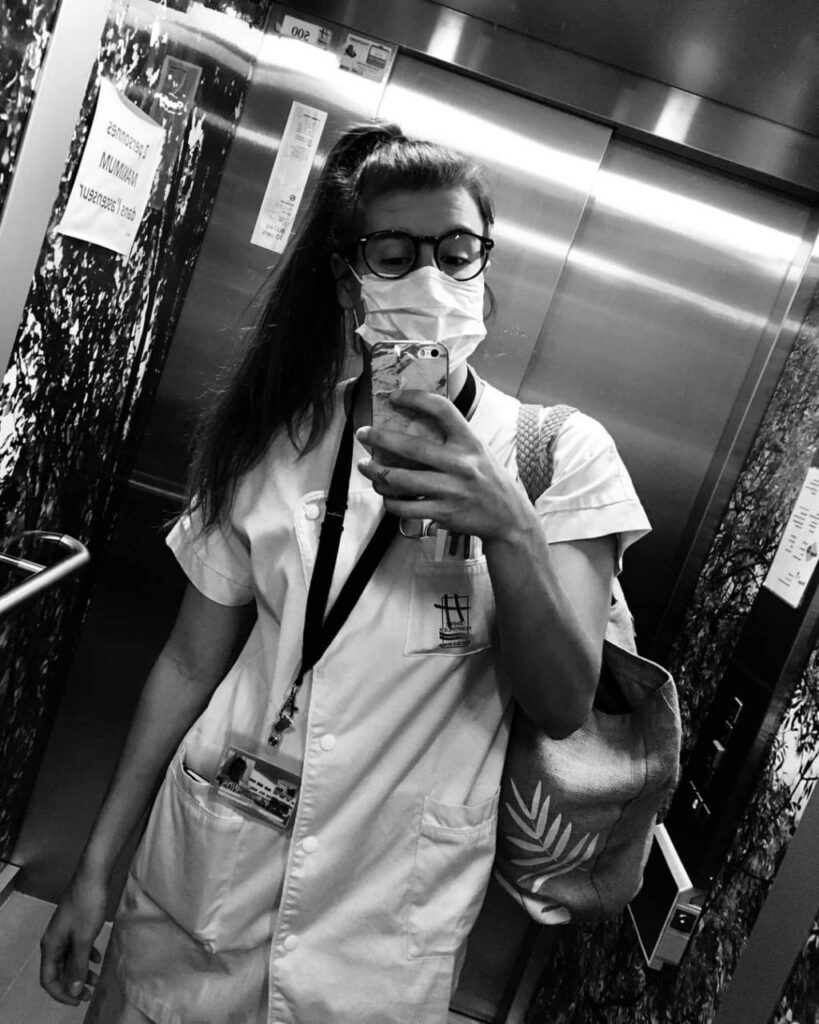 Photo de Lou Baranger, infirmière, en blouse et masque, dans un ascenseur
