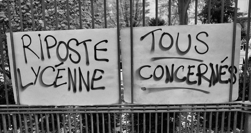 Photo en noir et blanc de Serge D'Ignazio : 
2 pancartes accrochées sur des grilles : "Riposte Lycéenne", "Tous concernés".