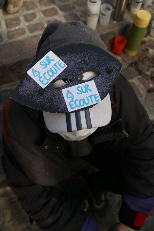 Photo de Dijoncter :
Une personne masquée portant 2 étiquettes "Sur écoute" sur son chapeau.