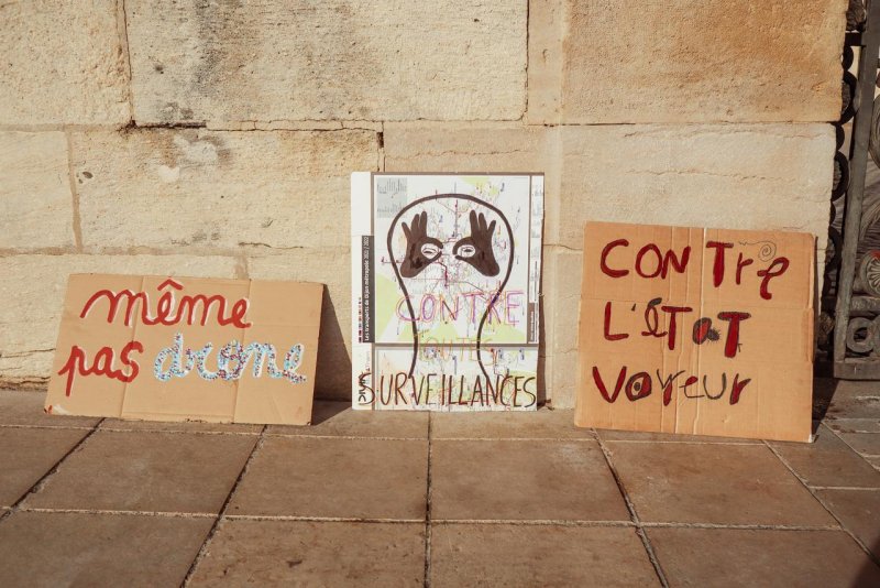 Photo de Dijoncter :
3 pancartes : 
"Même pas drone"
"Contre toutes les surveillances"
"Contre l'État voyeur".