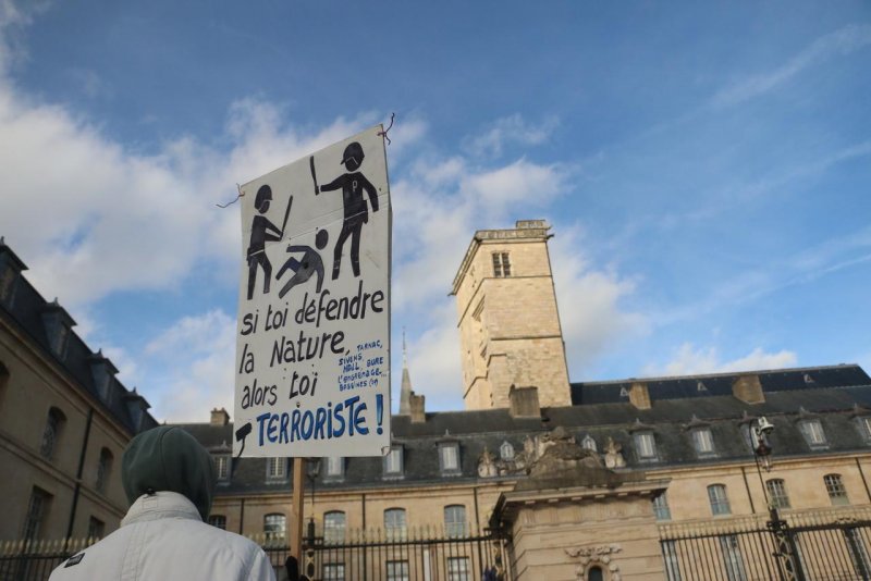 Photo de Dijoncter :
Une personne porte une pancarte sur laquelle 2 flics frappent une personne à terre, légende : "Si toi défendre la nature alors toi terroriste".