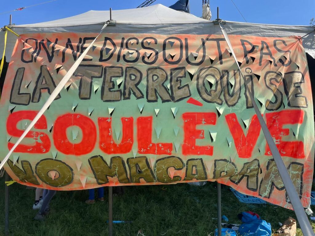 Photo de Gochopacontent. Grande banderole sur un barnum « On ne dissout pas la terre qui se soulève. No macadam »