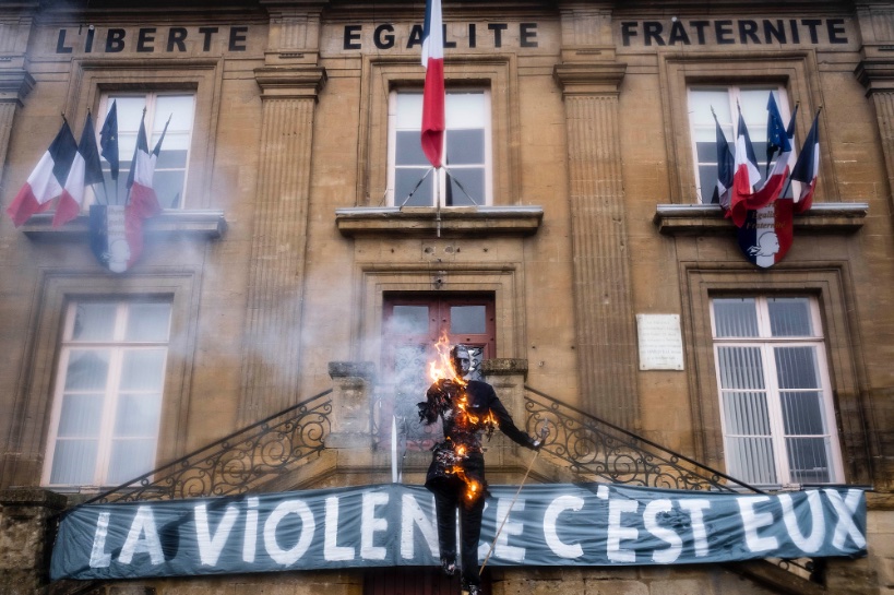 Photo (crédit inconnu) d'un pantin brûlé devant une Mairie, derrière lui une grande banderole sur laquelle est inscrit "La violence c'est eux."
