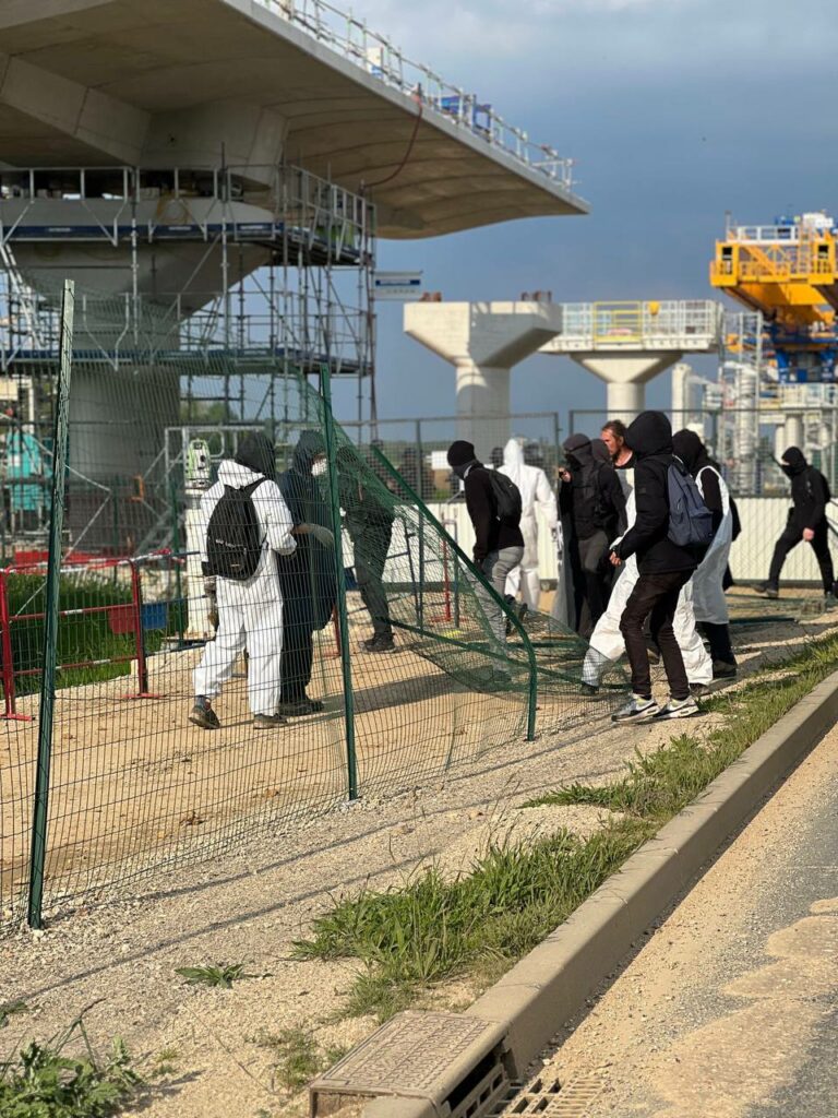 Photo du Collectif contre la ligne 18. On voit des militants habillés en combinaisons blanches ou tout en noir s'introduire sur un chantier.