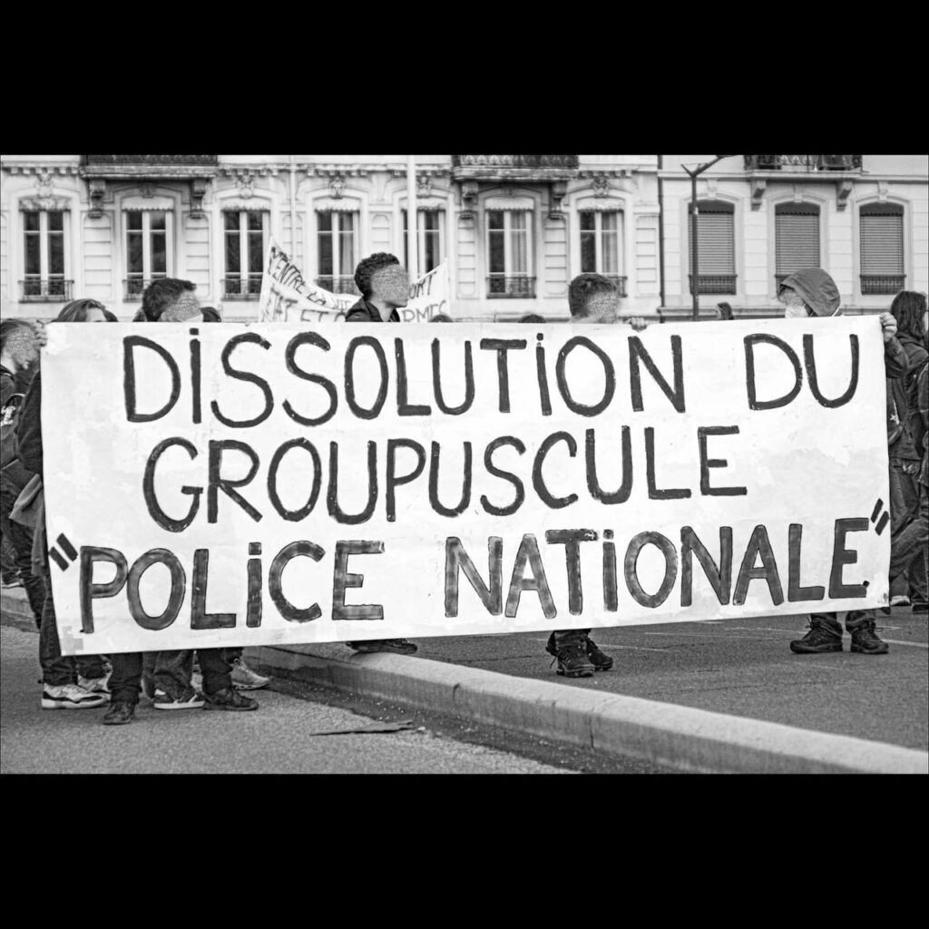 Photo de Lyon Insurrection. 
Photo en noir et blanc. Banderole en manif : "Dissolution du groupuscule Police Nationale".