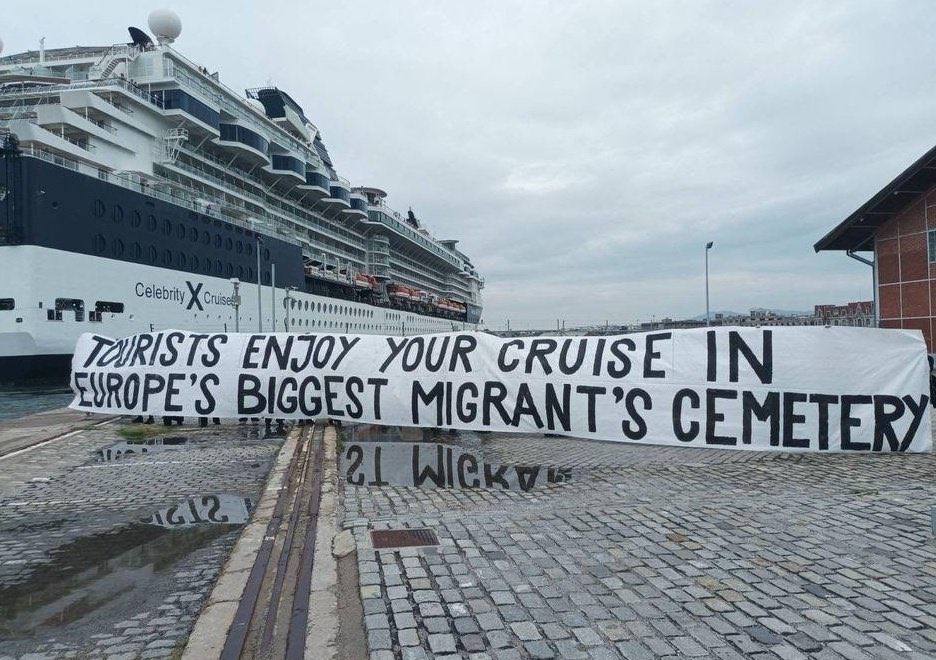 Photo d'Alexandros Kottis prise le 18 juin 2023 à Thessalonique en Grèce. Sur un port, devant un navire de croisière une grande banderole est déployée, son texte est en anglais : "Touristes profitez de votre croisière dans le plus grand cimetière de migrants d’Europe".