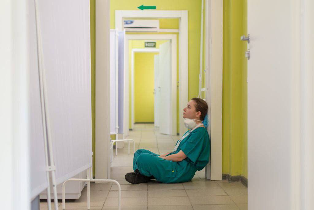 Photo via QGMédia. On voit une soignante assise seule dans un couloir. 