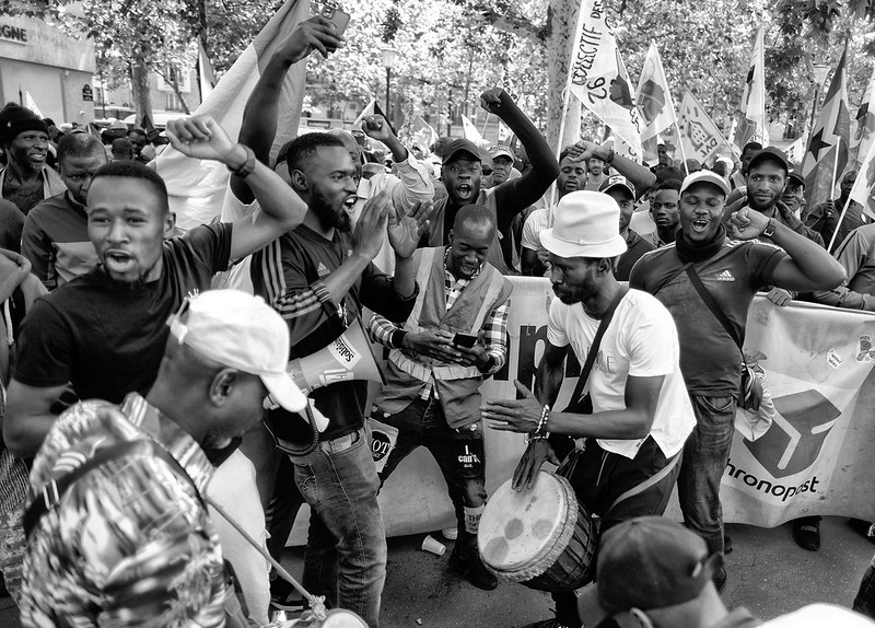 Photo de Serge D'Ignazio prise lors de la manifestation du 14 juillet 2023. Photo en noir et blanc. On voit un groupe dans le cortège en train de jouer de la musique, danser, chanter, certains avec le poing en l'air. 