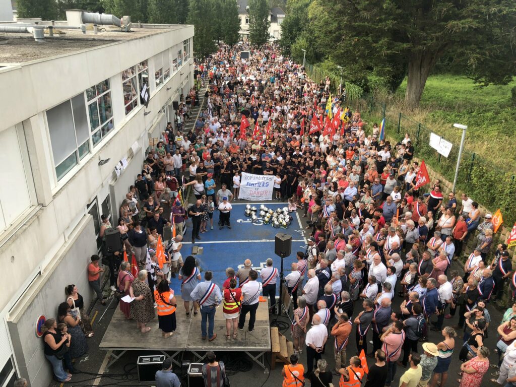 Photo de Ouest France où on voit de très nombreuses personnes rassemblées devant l'hôpital de Carhaix. La foule est tellement immense que la fin du cortège n'arrive pas à atteindre l'hôpital. On distingue notamment des chasubles des syndicats Cgt et Cfdt, des écharpes d'élus, des drapeaux politiques 