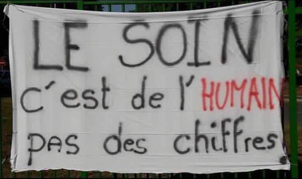 Photo d'une banderole en tissu blanc sur laquelle est écrit "LE SOIN c'est de l'HUMAIN pas des chiffres !"