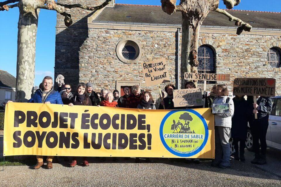 Photo prise lors d’une manifestation, on voit une grande banderole sur laquelle est noté « Projet écocides, soyons lucides ! » et le logo du Cri du bocage.