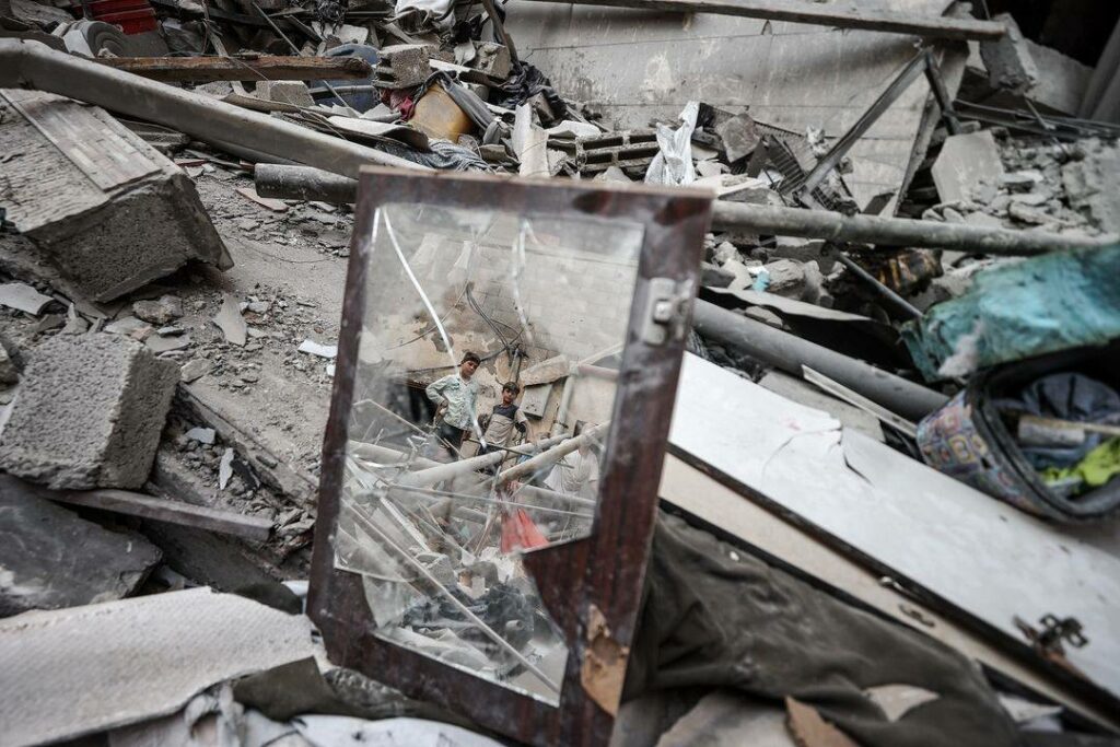 Photo d'Ali Jadallah prise dans le camp de réfugiés de Maghazi après les attaques israéliennes les 14 et 15 juillet. Des décombres. Au centre, un miroir brisé dans lequel se reflètent deux enfants qui regardent ce miroir. Le photographe explique que pendant ce temps, des Palestiniens cherchent des personnes et objets dans ce champ de ruines après que l'armée israélienne ait attaqué ce camp de réfugiés et d'autres à Deir-al-Balah.