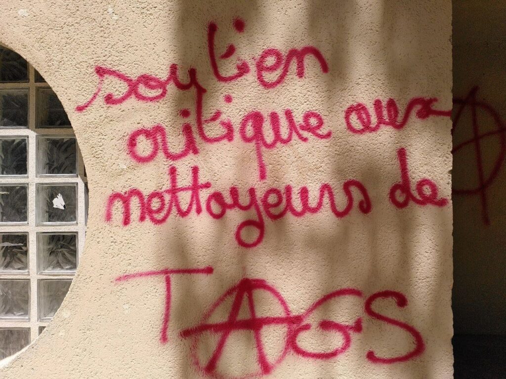 Tag écrit en rouge sur un mur : "Soutien critique aux nettoyeurs de tags". Le A de tags est le symbole de l'anarchie.